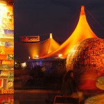 Frau sitzt vor der verlassenen Musik Arena. Um sie herum beleuchtete Kunstwerke.