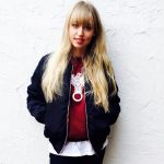 Veronika Bittenbinder mit Bomberjacke vor einer weißen Wand.