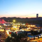 Ein Blick vom Olympiaberg über das festlich beleuchtete Tollwood Sommerfestival hinüber zum o2 Hochhaus