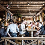 Oktoberfest Company Reservation - Tische mit Oktoberfestbesuchern rund um die Sektbar in Kufflers Weinzelt.