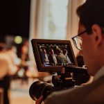 Auf einem Corporate Event dreht ein Kameramann. Im Vorschaubildschirm der Kamera sind Konferenzteilnehmer im Gespräch zu sehen.