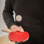 zu sehen ist wie Sascha Schloifer Tischtennis in der Hand spielt, in seiner rechten Hand hält er einen Tischtennisschläger und einen Tischtennisball der in der Luft fliegt