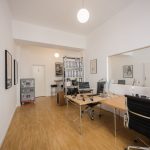 zu sehen ist die Agentur, zwei Arbeitsplätze, helle Räume, ein Regal mit Ordnern, Bilder hängen in dem ganzen Raum an der Wand