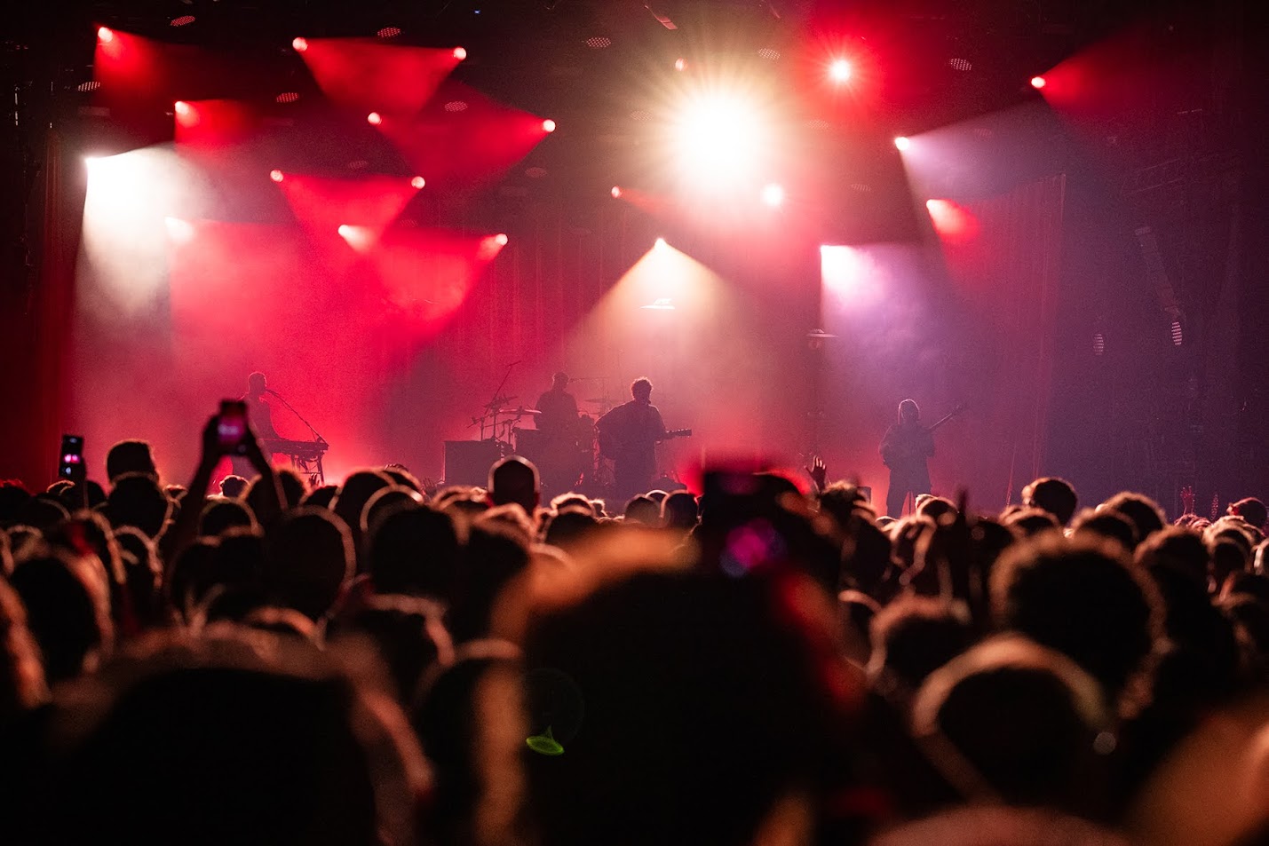 Studentenjobs in München: Bei vollblut arbeitest Du auf Konzerten in der Musik Arena. Das Bild zeigt ein die Bühne mit Publikum und Musikern. Die Veranstaltungs-Location ist rot ausgeleuchtet.