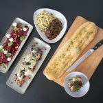 Das Foto zeigt folgende Gerichte von links nach rechts: Tonak Panna Cotta mit Bratapfel, Beetroot Burratina, Ragout vom bayerischen Weiderind mit Preiselbeersauce und Spätzle, eine hausgemachte Focaccia und eine Aprikosen-Rosmarin Creme