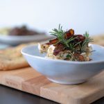 Das Bild zeigt eine Aprikosen-Rosmarin Creme und eine Focaccia. Im Hintergrund sind verschwommen weitere Speisen zu sehen.