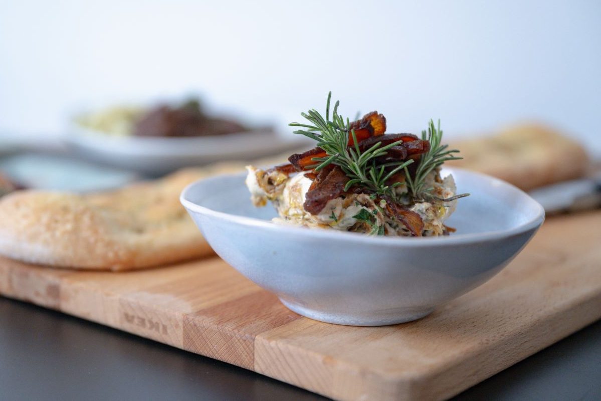 Das Bild zeigt eine Aprikosen-Rosmarin Creme und eine Focaccia. Im Hintergrund sind verschwommen weitere Speisen zu sehen.