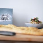 Das Bild zeigt die Titelmotiv der Menükarte aus dem Hexenkessel, sowie eine Aprikosen-Rosmarin Creme und eine hausgemachte Focaccia. Aufgenommen wurde das Bild im Rahmen eines Probeessens für die neuen Bio-Buffets 2024, die ab sofort über vollblut LiveMarketing für Gruppen und Firmenweihnachtsfeiern buchbar sind.