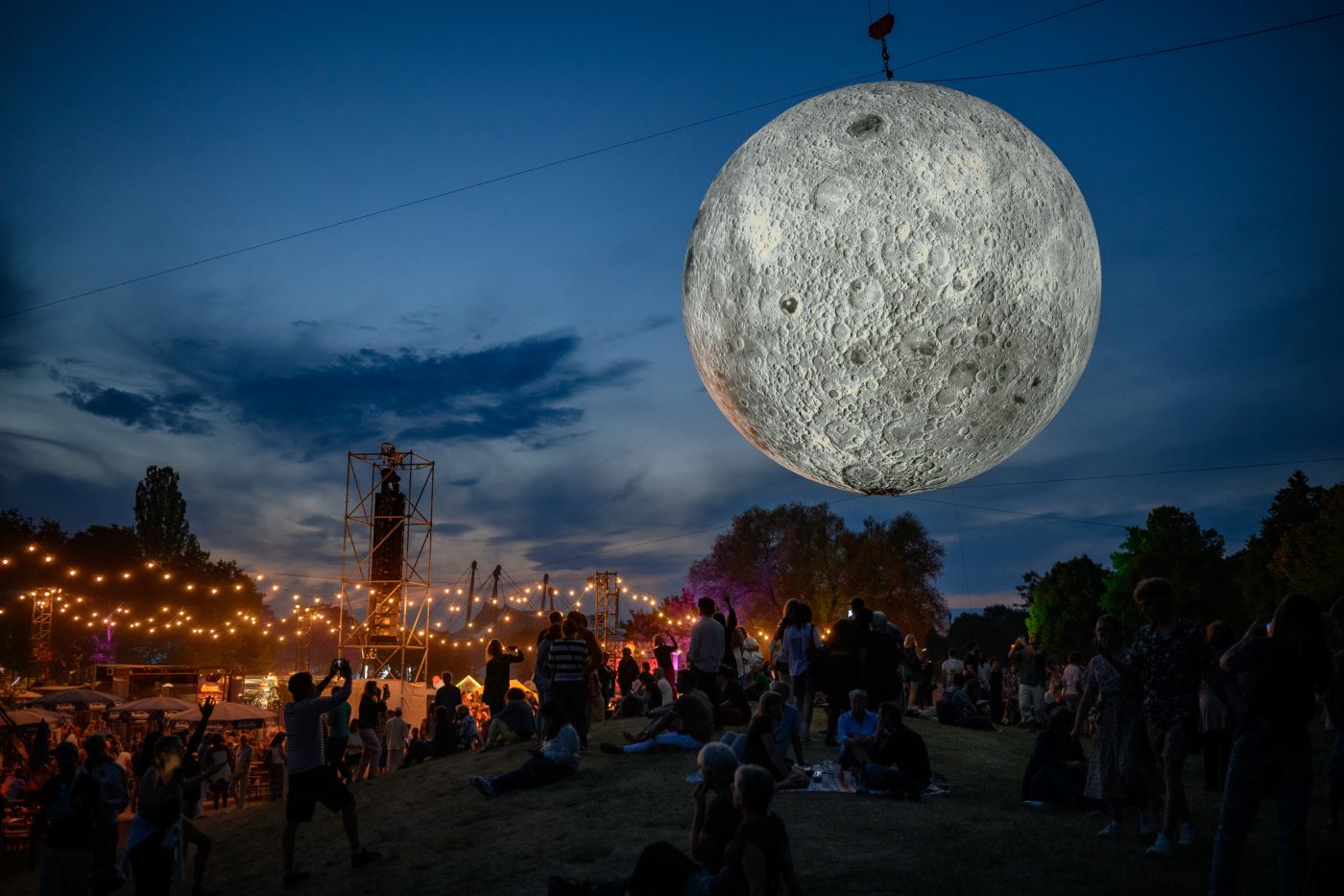 Studentenjob in München Veranstaltungsbetreuer: Das Bild zeigt das Tollwood Festival kurz bevor die Sonne komplett untergegangen ist und zeigt einen installierten Mond, der scheinbar ganz nah über dem Festival schwebt.